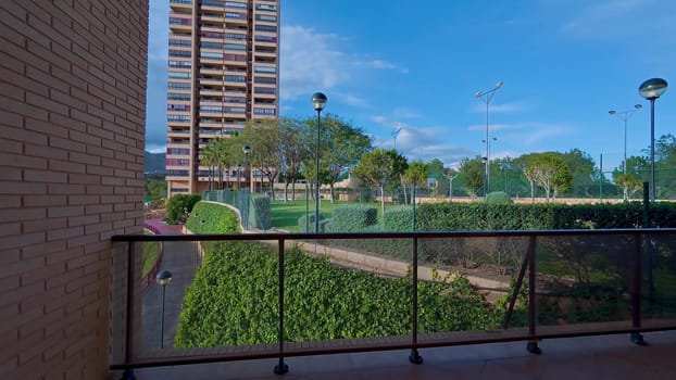 A modern balcony view overlooking a vibrant urban park with greenery and a stylish residential building