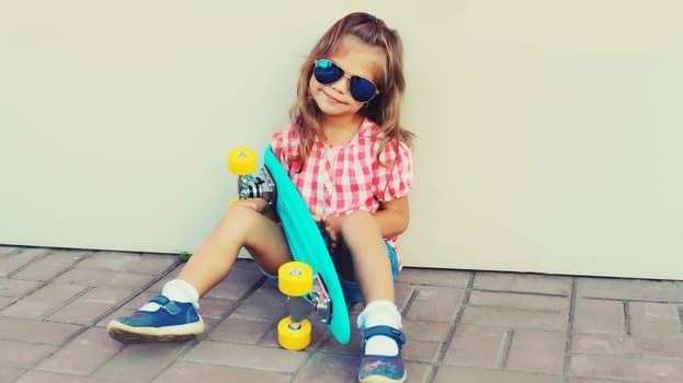 Portrait of stylish little girl child posing with skateboard on city street
