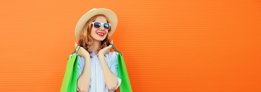 Fashion, purchase. Portrait of stylish beautiful happy young woman posing with colorful shopping bags, girl in summer hat standing on bright orange background