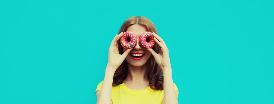 Portrait of happy cheerful smiling young woman with sweet donut having fun isolated on blue studio background