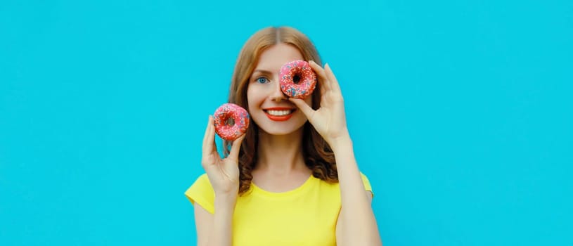 Portrait of happy cheerful smiling young woman with sweet donut having fun isolated on blue studio background