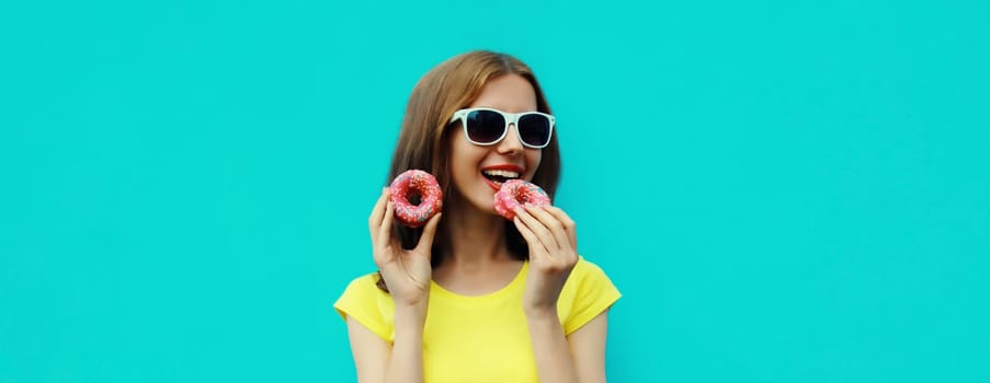 Portrait of happy cheerful smiling young woman with sweet donut having fun isolated on blue studio background