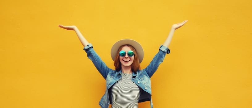 Summer holidays, inspired happy cheerful smiling young woman raising her hands up wearing denim clothing, straw hat on colorful yellow background
