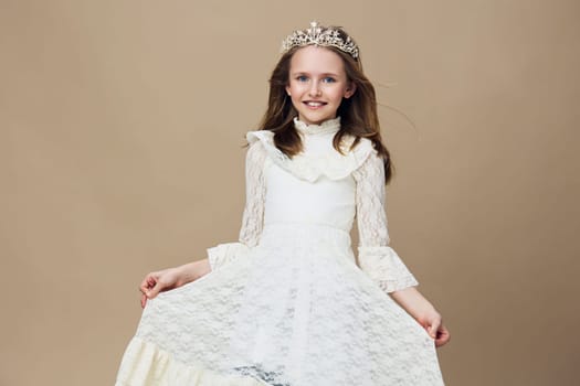 A joyful young girl wearing a stunning white dress and a tiara, exuding happiness against a soft beige background, ideal for themes of childhood, elegance, and special occasions