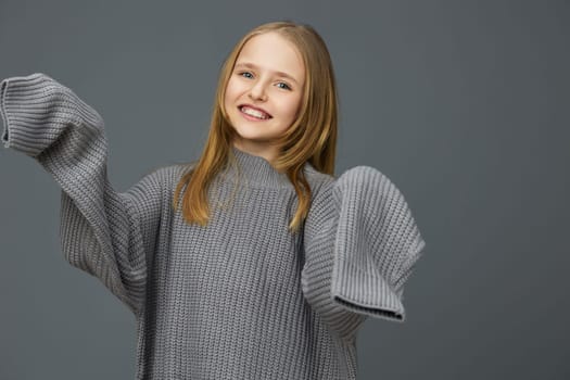 Happy girl wearing an oversized grey knitted sweater smiles joyfully against a simple grey background, ideal for autumn fashion themes and cozy lifestyle concepts