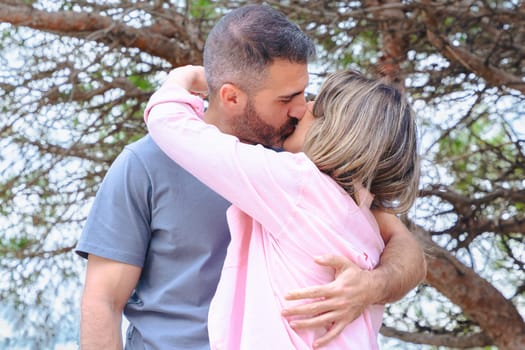 Loving couple sharing a passionate kiss under a tree in a natural setting. Tender moment full of emotion, intimacy, and connection, framed by branches and daylight in a calm outdoor scene.
