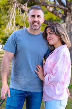 Vertical portrait Young couple standing together outdoors, gazing into each other's eyes with love. Natural park environment, sunshine, green grass, and peaceful mood highlighting emotional connection