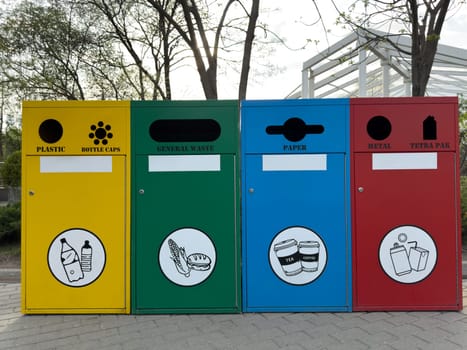 Colorful recycling bins for plastic, general waste, paper, and metal stand side by side in an urban park, promoting environmental responsibility and sustainable waste separation