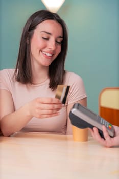 African American and Caucasian women smiling while paying at a coffee shop. One holds a card, the other a phone. Concept of friendship, technology, and casual lifestyle in a modern setting. Vertical