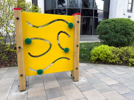 Educational outdoor toy for children in park. Bright yellow maze panel promoting coordination, logic and fine motor skill development through interactive play