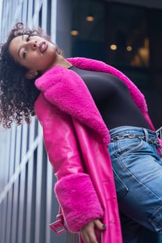 African american dancer with curly hair wearing a pink coat, expressing movement and energy in an urban environment. Modern fashion, contemporary dance,and artistic performance against a city backdrop