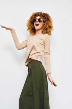 Bright and cheerful fashion portrait featuring a woman with curly hair wearing a stylish beige top and green skirt She is smiling and enjoying herself against a clean, neutral backdrop