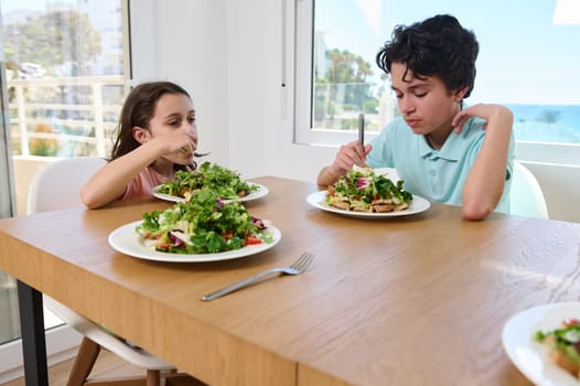 Two children are seen enjoying a nutritious meal featuring fresh salad in a bright, modern kitchen as sunlight fills the room, creating a serene and healthy ambiance.