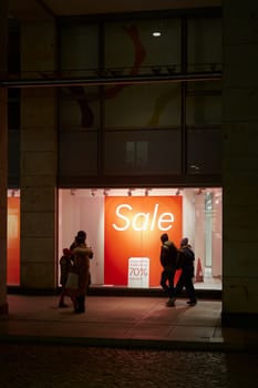 Dresden, Germany – January 18, 2025: Passers-by window shopping in the evening and a sign with the inscription Sale