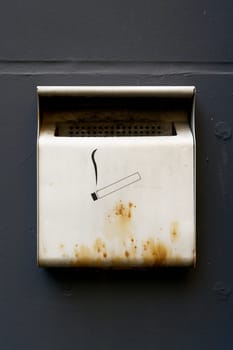 Container for cigarettes, ashtray on a house wall at a smoking area
