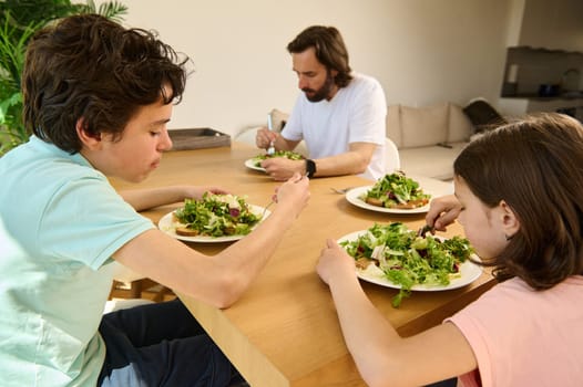 A family sits at a wooden table in a modern home, enjoying a vegetarian meal together. They share a healthy and intimate dining experience, showcasing bonding over nutritious food.