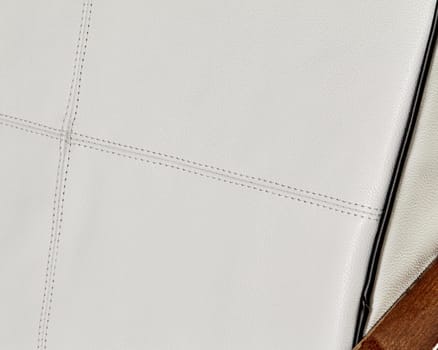 Close-up of white leather upholstery featuring prominent stitching, forming a geometric pattern, ideal for backgrounds related to furniture, design, or craftsmanship