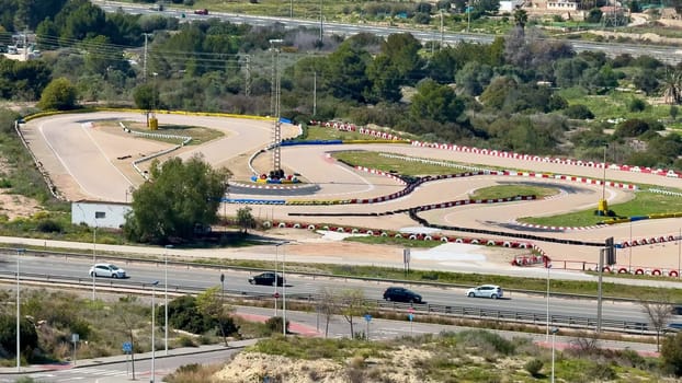 Scenic aerial view of a vibrant gokart track with vehicles, surrounded by lush greenery and a winding road