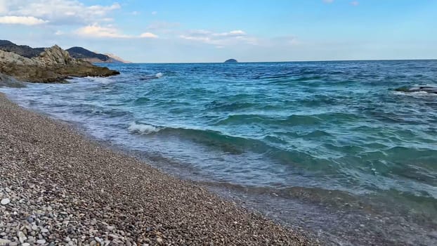 A truly stunning coastal view showcasing gentle waves lapping at a pebbly beach beneath a clear, sunny blue sky