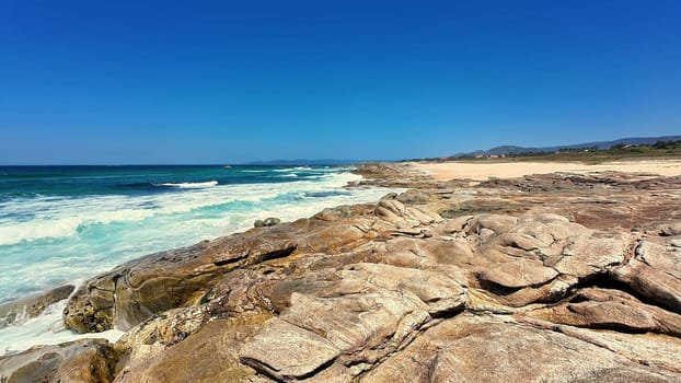 An enchanting coastal scene showcasing majestic rocks, gentle ocean waves, and a beautifully clear blue sky