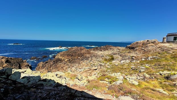 A breathtaking coastal landscape featuring rugged, jagged rocks alongside the shimmering blue ocean beneath a clear sky