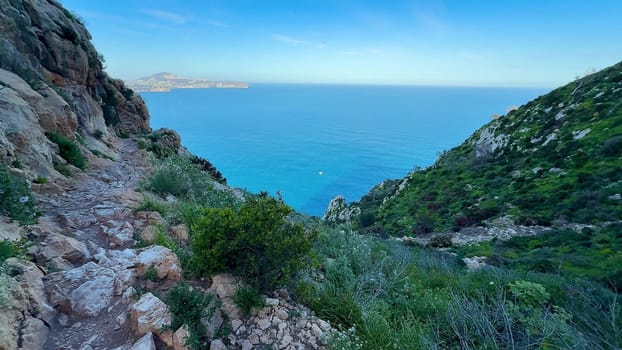 A breathtaking view of a rugged, rocky coastal trail adorned with lush greenery and an expansive ocean horizon