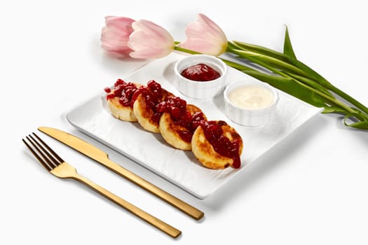 Delicious syrniki served with jam and sour cream, garnished with pink tulips, creating an appetizing culinary scene