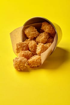 Popcorn chicken spilling out of a metal bucket onto a vibrant yellow backdrop, creating a visually appealing fast food scene