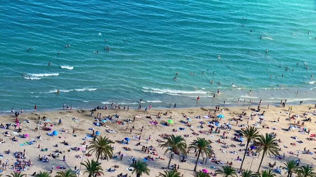 Aerial view of a beach scene with sunbathers enjoying turquoise waters and swaying palm trees in a light breeze