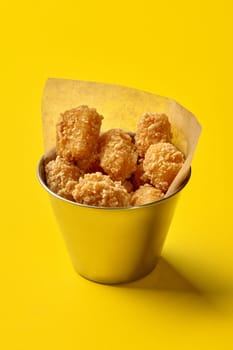 Breaded tater tots overflowing a metal bucket on a vibrant yellow background, creating a visually appealing fast food scene