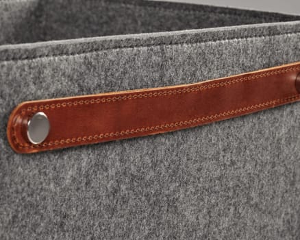Close-up of brown leather handle attached with metal rivet on grey felt storage basket, highlighting modern and minimalist design