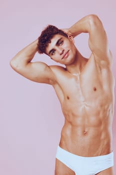 Fit male model with curly hair, smiling while holding hands behind head, highlighting strength and confidence. Ideal for fitness and lifestyle themes.