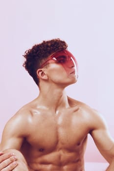 Confident young man with well-defined muscles and stylish curly hair, wearing a vibrant red visor. The soft pink background enhances the modern fashion and self-expression vibe.