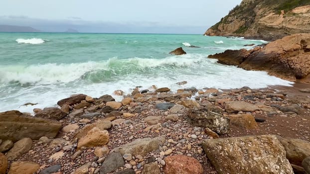 A breathtaking and stunning view of powerful waves crashing against a rugged rocky shoreline under a cloudy sky