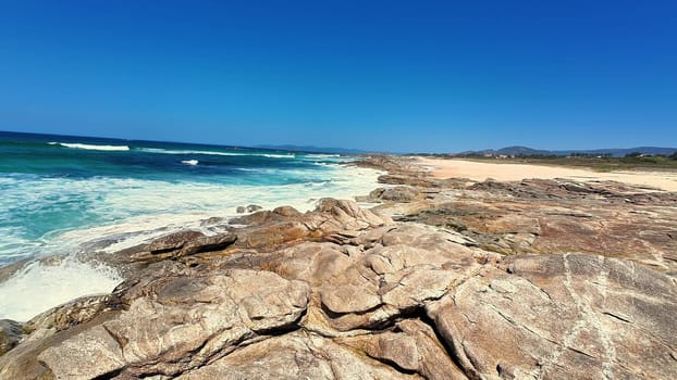 The stunningly beautiful view of the rugged rocky coast features clear blue skies and ocean waves crashing