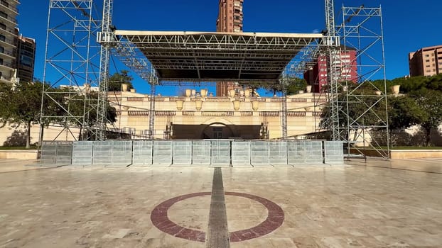 A beautifully prepared concert stage is set amidst city buildings, all under a bright and clear blue sky