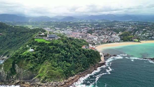 This breathtaking aerial shot captures a gorgeous coastal area with a vibrant green hill and a tranquil beach