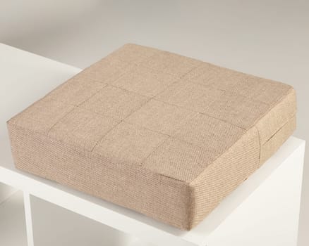 Square beige fabric padded seat cushion resting on a white shelf, offering comfort and style