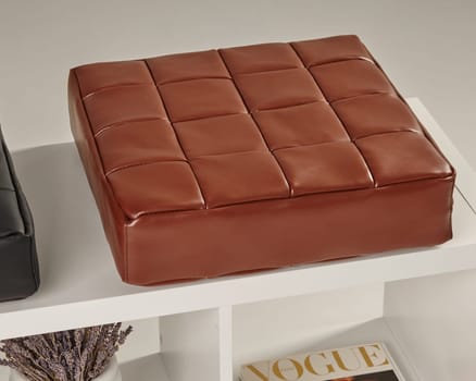 Square brown leather pouf resting on a white modern shelf, creating a stylish and comfortable seating arrangement