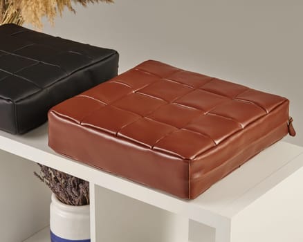 Square, woven leather cushions sit on a white shelf, adding a touch of elegance to a minimalist interior design