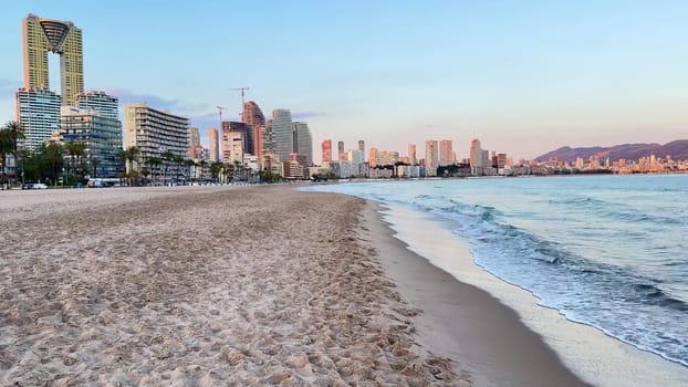 Captivating beach scenery featuring soft gentle waves, a picturesque city skyline, and beautiful serene sunset colors