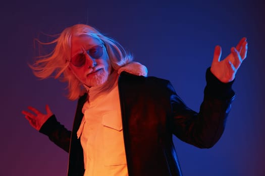 A fashionable man with long white hair and sunglasses stands confidently, dressed in a black leather jacket, set against a vibrant blue and red background, exuding a dynamic and modern vibe