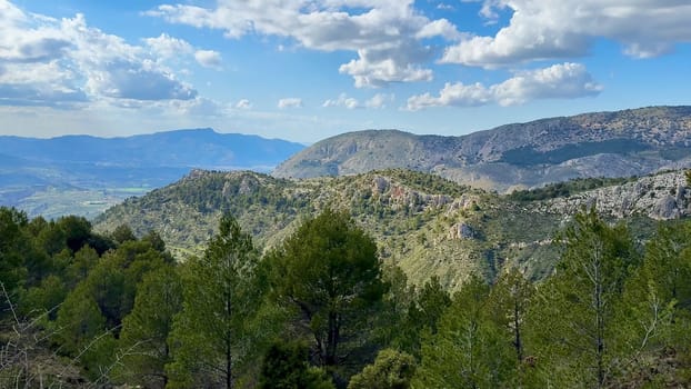 A stunning panoramic view of majestic mountains, lush greenery, and fluffy clouds under a clear blue sky