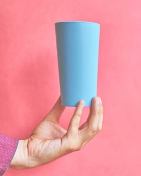 Colorful plastic cup. Plastic blue cup in hand on pink background.