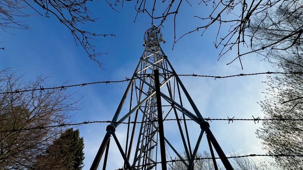 A striking and captivating view of a large communication tower secured tightly by barbed wire against a clear blue sky