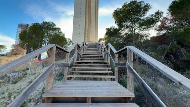 A beautifully crafted wooden staircase gracefully ascends towards a tall and impressive tower, surrounded by lush trees