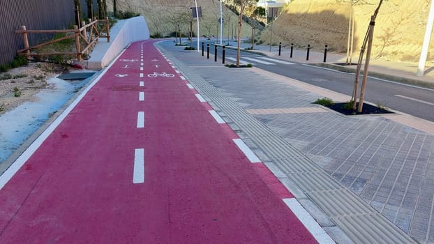 A pink bike lane winds through a bustling urban area, next to a landscaped path filled with lush trees