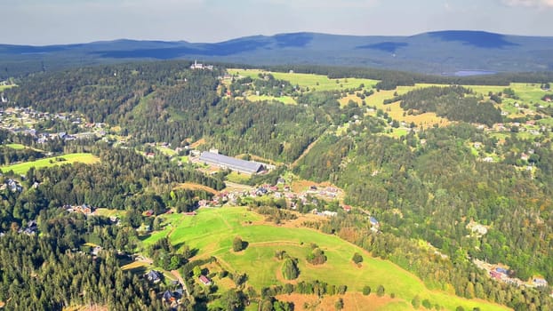 A stunning aerial perspective showcases lush green hills alongside serene mountains stretching beneath a clear sky