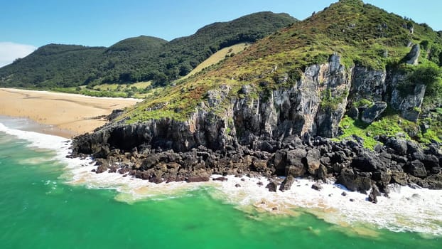 Experience breathtaking views of green hills, rocky cliffs, and a serene beach on a perfect sunny day
