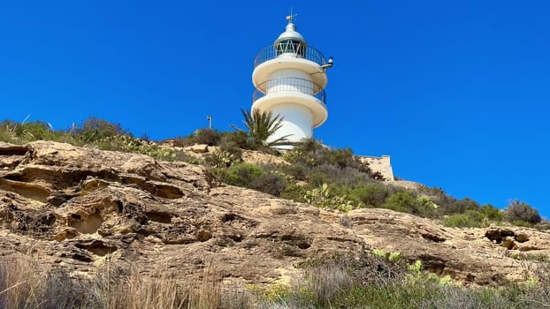 A stunning lighthouse perched on a rocky hillside, surrounded by lush vegetation and a vibrant blue sky.